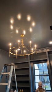 An electrician installing a chandelier with a ladder in a home by Camo Construction & Electric in Lake Charles, LA.