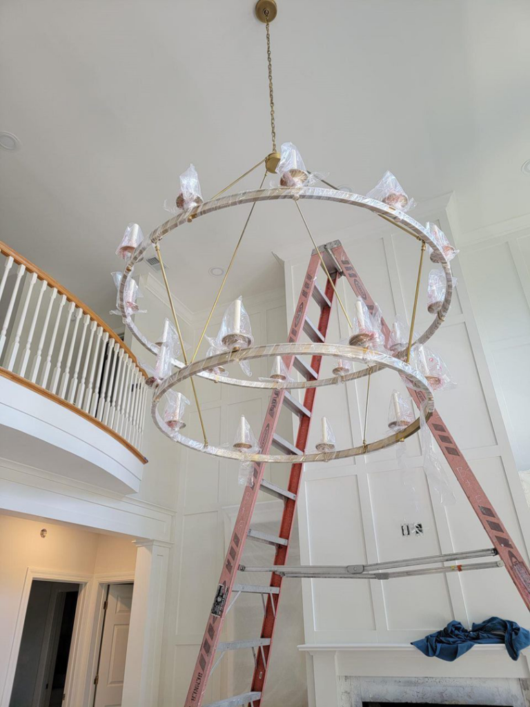 Electrician installing a large chandelier in a high-ceiling foyer by D&R Construction & Electrical Services in Summerville, SC.