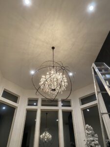 Electrician installing a large chandelier in a high-ceiling room with a ladder by Volt Electric LLC in Nampa, ID