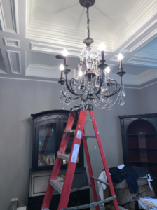 An electrician's ladder positioned under a chandelier, indicating installation or repair by Vera Electric in Aurora, IL.