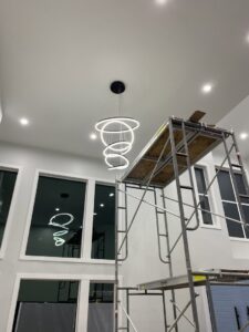 Electricians from Good Contact Electric, LLC installing a large modern chandelier using scaffolding in Tacoma, WA.