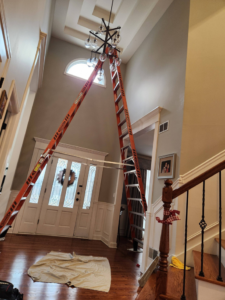 A chandelier being installed using two tall ladders in a high-ceiling entryway by Ed's Electrical & Mounting services in Chicago, IL.