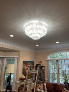 An electrician installing a large chandelier using a ladder for Armenergo Electrician in Rockville, MD
