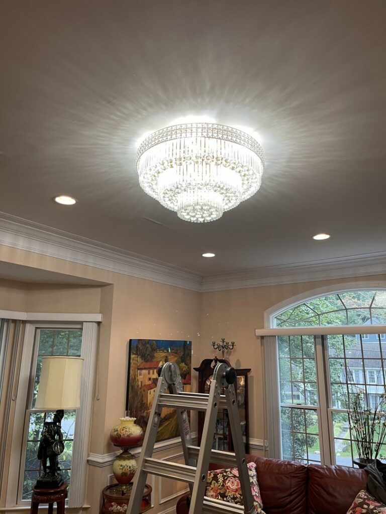 An electrician installing a large chandelier using a ladder for Armenergo Electrician in Rockville, MD