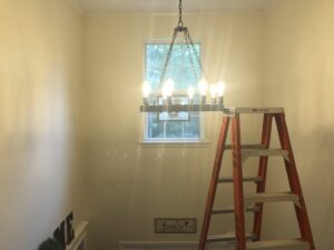 An electrician installing a chandelier with an orange ladder in a home by Omni Electrical Services LLC in Philadelphia, PA.