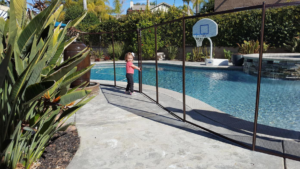 A child safely standing next to a removable mesh pool fence installed by Baby Guard Pool Fence Los Angeles, CA