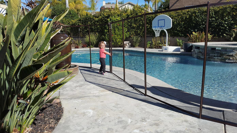 A child safely standing next to a removable mesh pool fence installed by Baby Guard Pool Fence Los Angeles, CA