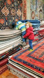 Children playing among the colorful stacks of tribal rugs at Yayla Tribal Rugs, Inc. in Cambridge, MA.
