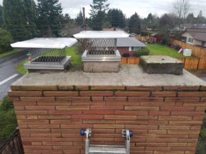 Two new metal chimney caps installed on a brick chimney with a ladder, by Matchbox Chimney Sweeps in Vancouver, WA.