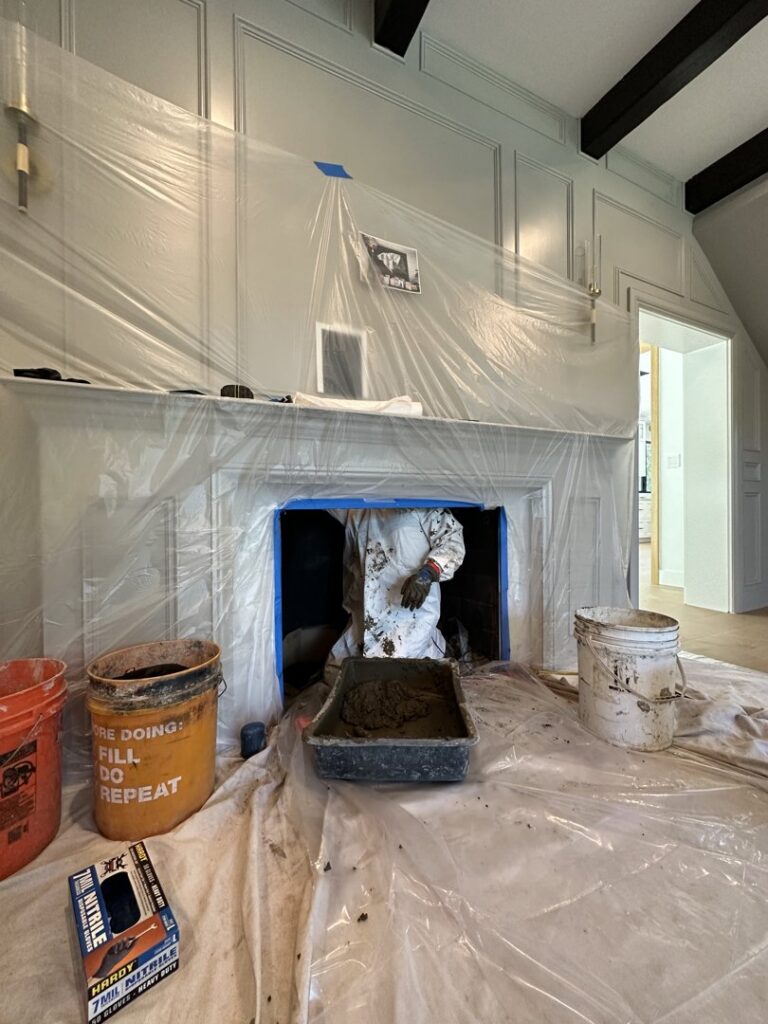 A worker in a protective suit performing chimney cleaning or repair inside a fireplace for The Chimney Guy in Los Angeles, CA.