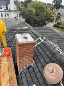 A Certified Masons worker on a roof installing chimney flues on a brick chimney in Warwick, RI