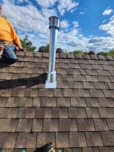 A worker on a roof installing a metal chimney flue and cap for JJ Chimney Services in Minneapolis, MN.