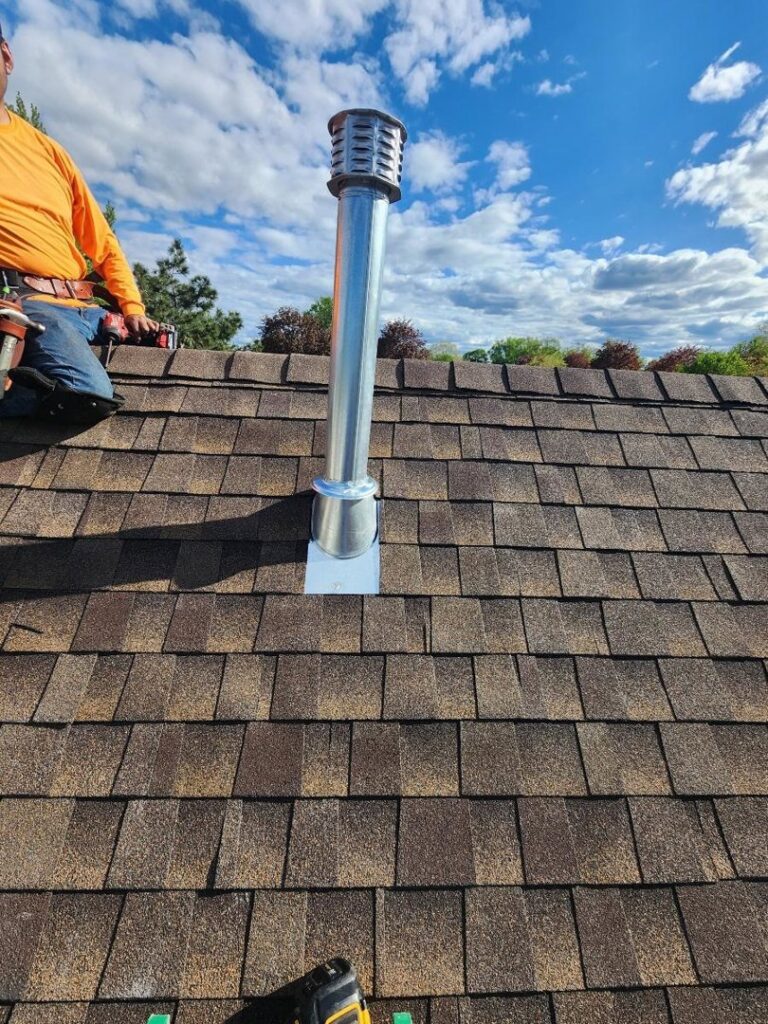A worker on a roof installing a metal chimney flue and cap for JJ Chimney Services in Minneapolis, MN.