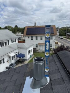 A metal chimney flue pipe being installed on a roof with a level by Certified Masons in Warwick, RI