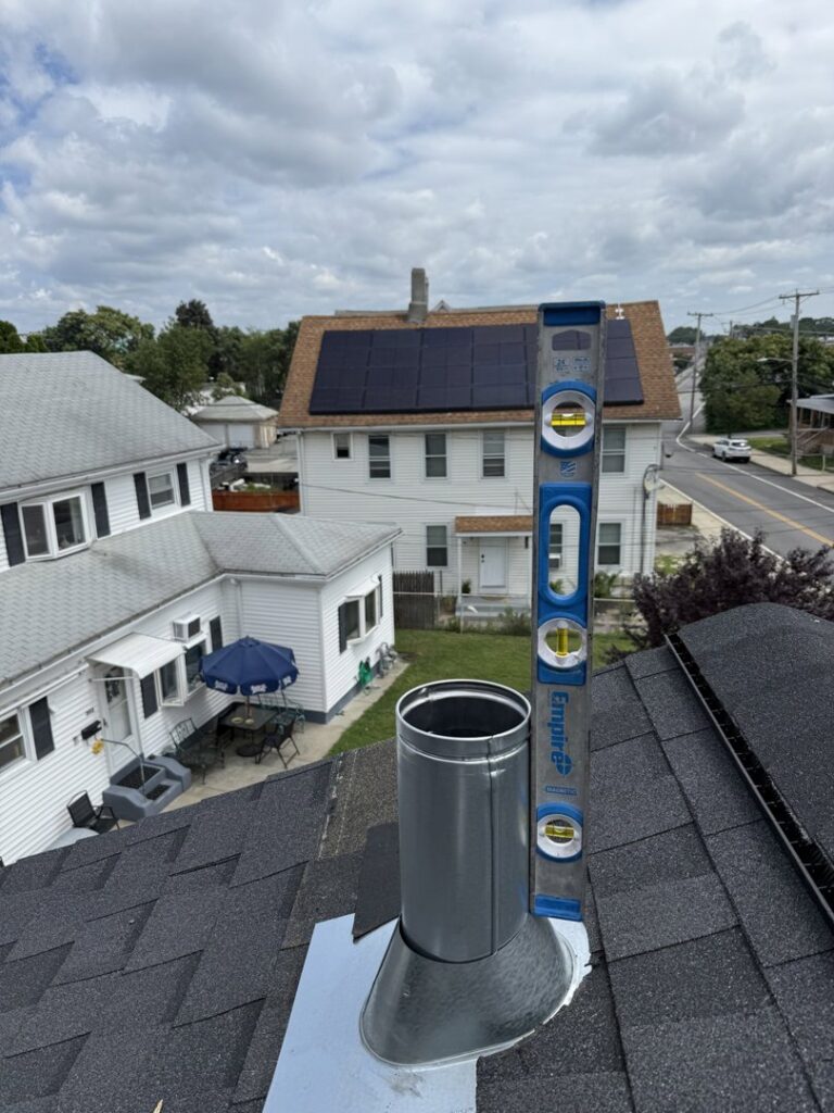 A metal chimney flue pipe being installed on a roof with a level by Certified Masons in Warwick, RI