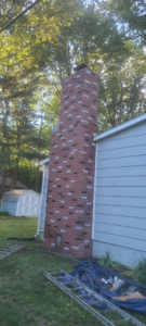 A tall brick chimney on the side of a house with a ladder leaning against it, ready for inspection or sweeping by Carl's Hearth Services in Feura Bush, NY.