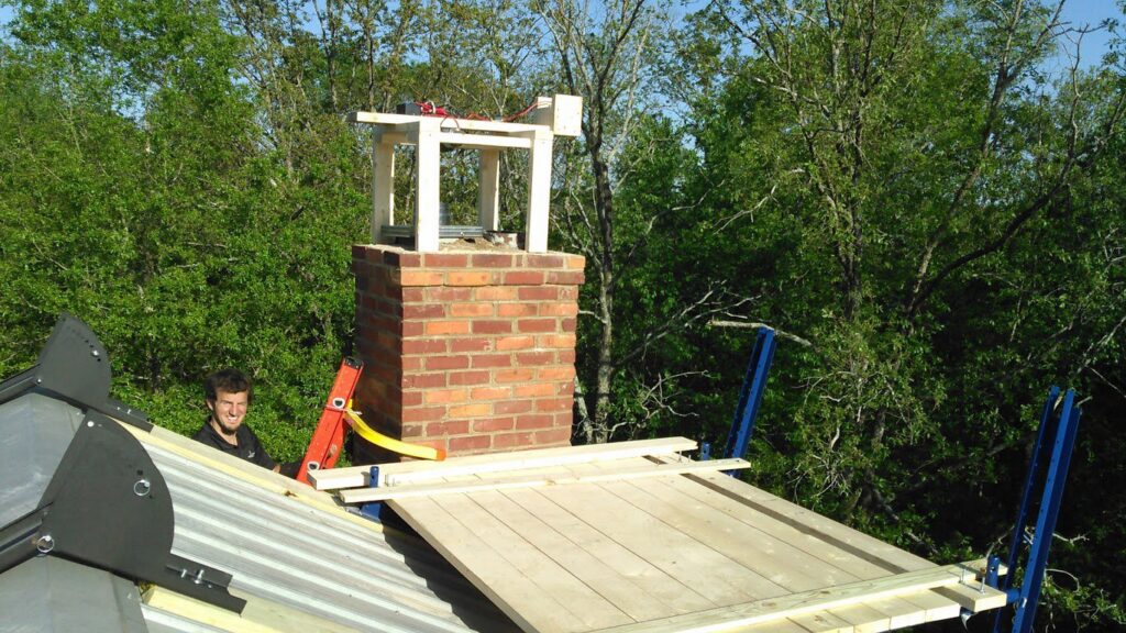 A chimney technician performing an inspection or repair on a brick chimney from a rooftop for Chip's Chimney in Rapid City, SD