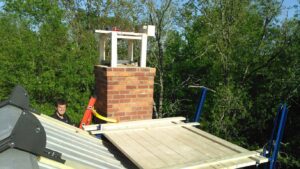A chimney technician performing an inspection or repair on a brick chimney from a rooftop for Chip's Chimney in Rapid City, SD
