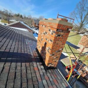 A brick chimney on a residential roof with scaffolding, showing masonry repair work in progress by The Chimney Doctor in Louisville, KY.