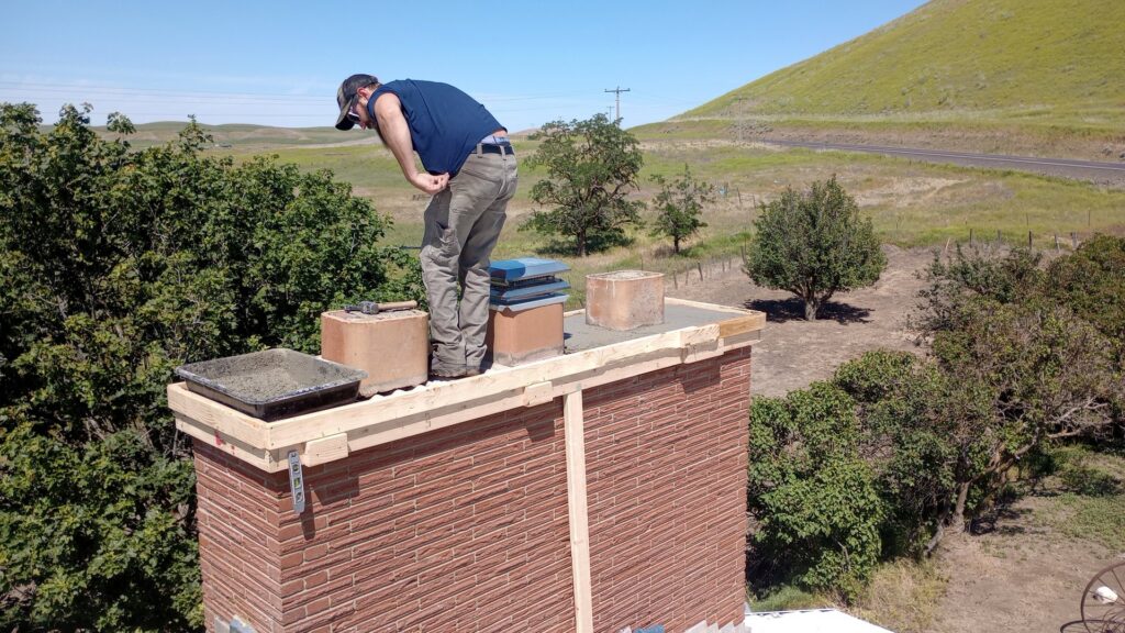 A chimney masonry repair worker on top of a brick chimney for Western Expanse Chimney and Hearth in De Smet, ID.