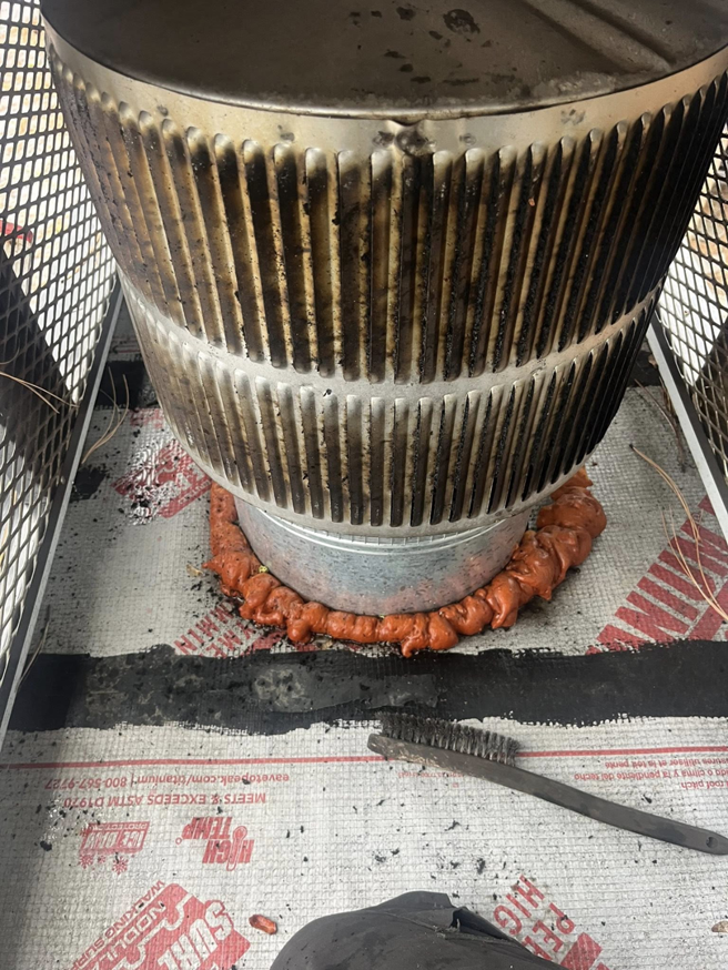 A chimney pipe on a roof with sealant and a cleaning brush nearby, indicating work by Heartland Chimney Sweeps LLC in McCall, ID.