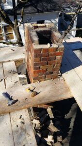 A brick chimney undergoing reconstruction or repair on a rooftop by Chip's Chimney in Rapid City, SD