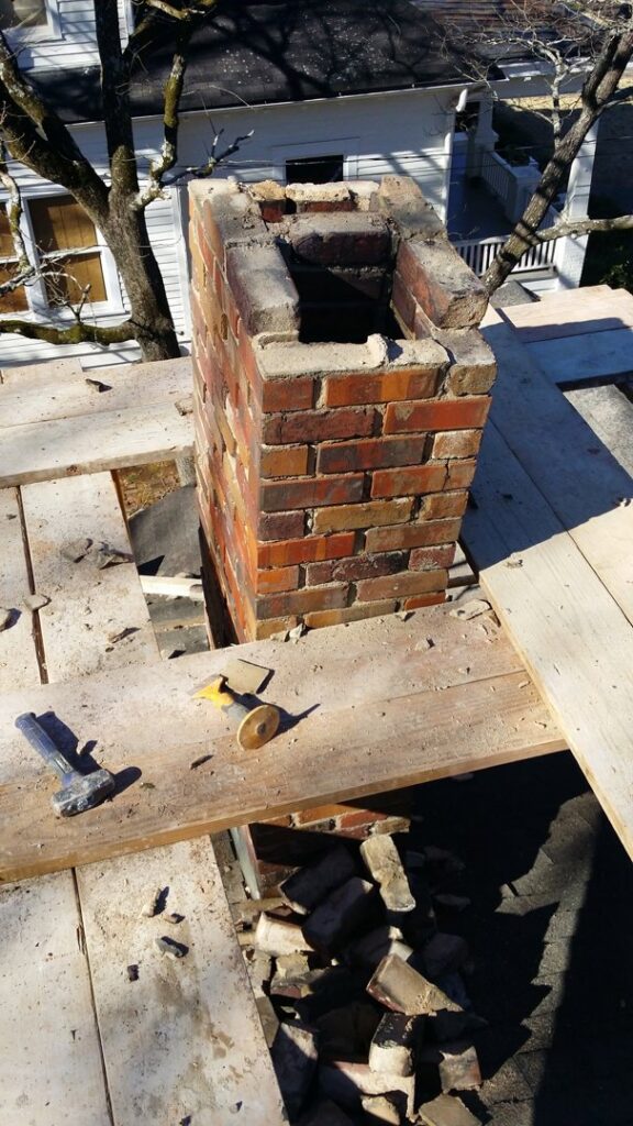 A brick chimney undergoing reconstruction or repair on a rooftop by Chip's Chimney in Rapid City, SD