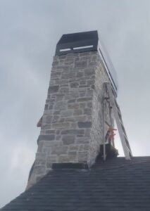 A professional working on a stone chimney on a roof, providing services from Professional Fireplaces and Chimney Sweeps in Huntsville, AL.