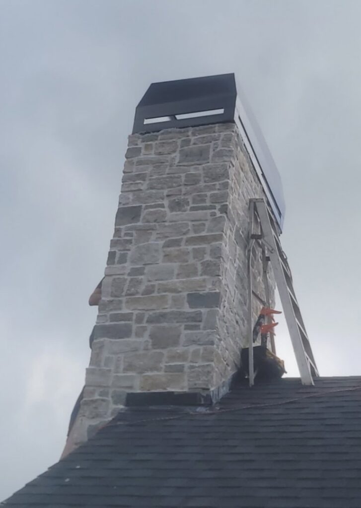 A professional working on a stone chimney on a roof, providing services from Professional Fireplaces and Chimney Sweeps in Huntsville, AL.