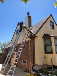 A Midtown Chimney Sweeps technician on a ladder performing chimney repair or installation work on a roof in Golden, CO.