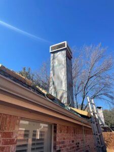 A chimney under repair or construction, wrapped in protective material with a ladder, by HBR Hearth and Chimney in Dallas, TX