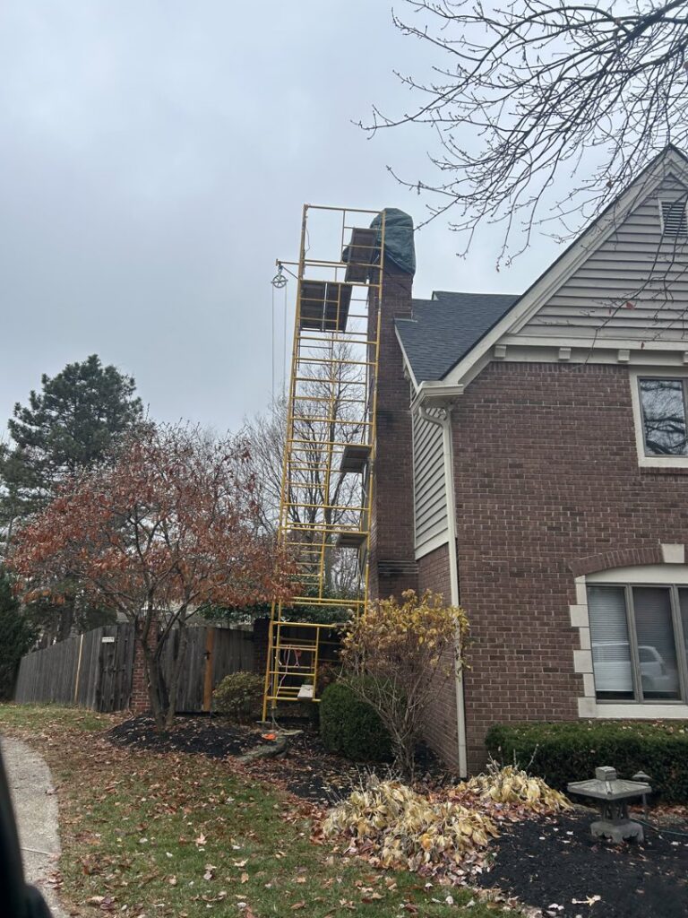 Scaffolding set up next to a brick chimney on a residential home, indicating chimney maintenance or repair by Indy Ignited in Indianapolis, IN.