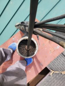 A chimney sweep brush inside a flue with chimney rods on a roof, performed by F.G Chimney & Service Repair & Sweep in Baltimore, MD.