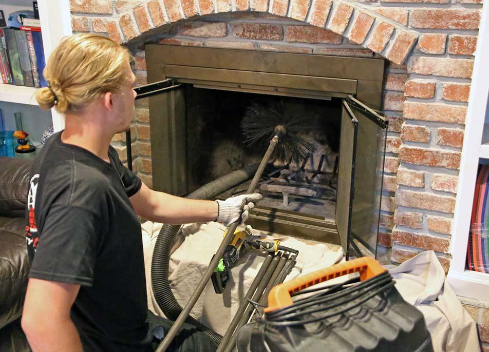 A chimney sweep technician from 832 Home Service using a brush and vacuum to clean a fireplace in Houston, TX.