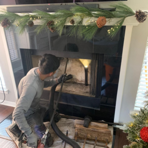 A technician from 832 Home Service cleaning the inside of a fireplace with a vacuum during a chimney sweep job in Houston, TX.