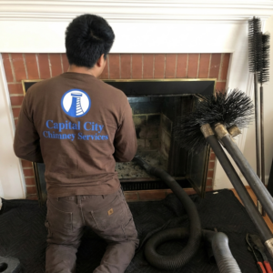 A chimney sweep from Capital City Chimney Services cleaning a fireplace with a vacuum and brushes in Austin, TX