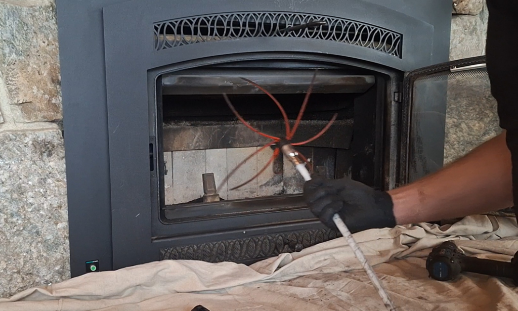 A chimney sweep cleaning a fireplace insert with a rotary brush at Western Expanse Chimney and Hearth in De Smet, ID.