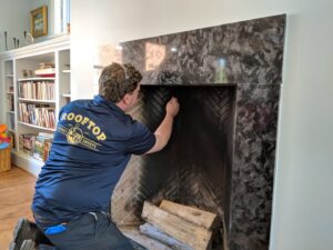 A chimney sweep technician cleaning the interior of a fireplace for Rooftop Chimney Sweeps in Alexandria, VA.