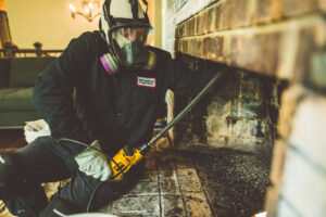 A chimney sweep from Soot Busters in a respirator, thoroughly cleaning the interior of a fireplace in Birmingham, AL.
