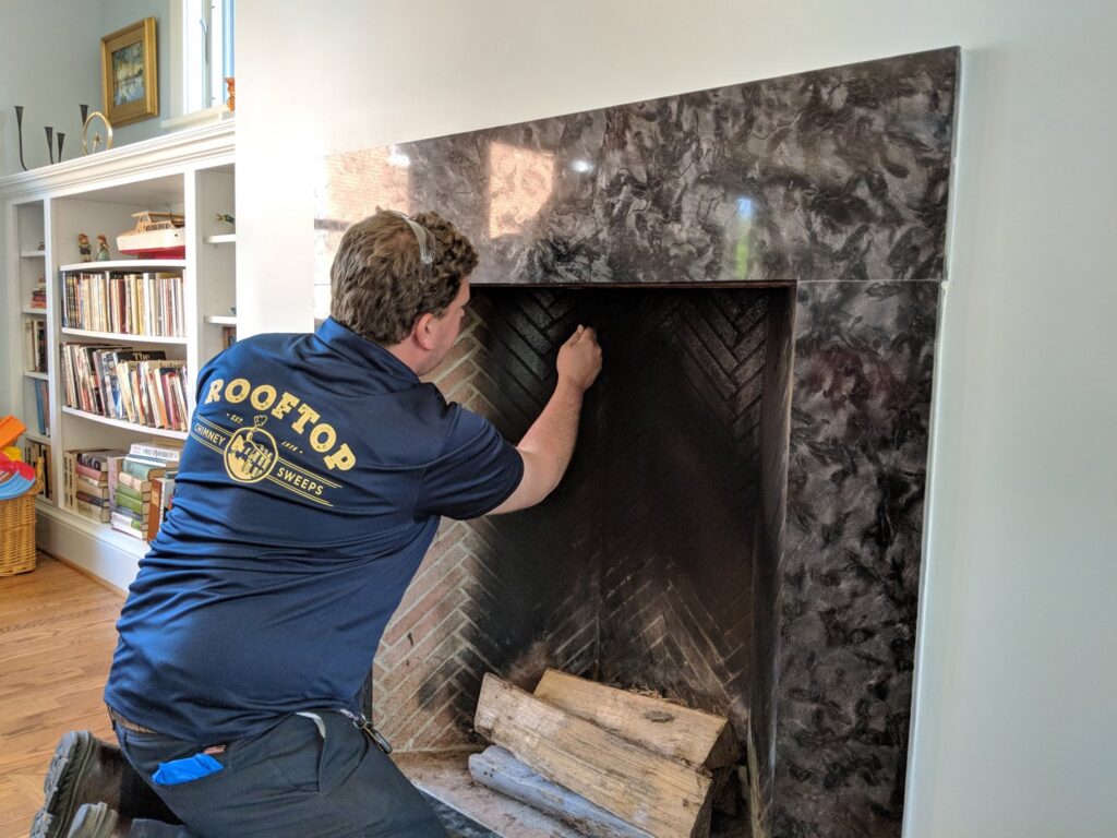 A chimney sweep technician cleaning the inside of a fireplace for Rooftop Chimney Sweeps in Alexandria, VA.