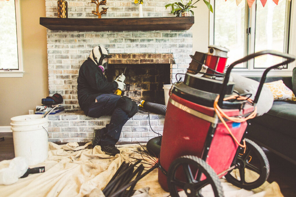 A chimney sweep from Soot Busters wearing a respirator while cleaning a fireplace with specialized equipment in Birmingham, AL.