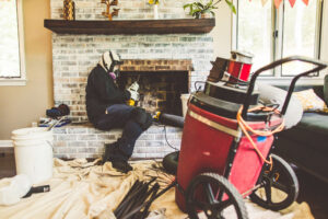A chimney sweep from Soot Busters wearing a respirator while cleaning a fireplace with specialized equipment in Birmingham, AL.
