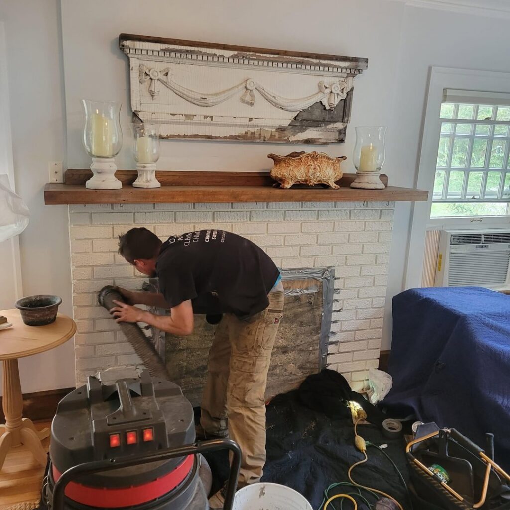 A chimney sweep cleaning a fireplace interior with a large industrial vacuum cleaner at a client's home by Century Chimney Sweep and Repair in Cleveland, OH