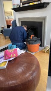 A chimney sweep technician cleaning a fireplace with a vacuum for Rooftop Chimney Sweeps in Alexandria, VA.