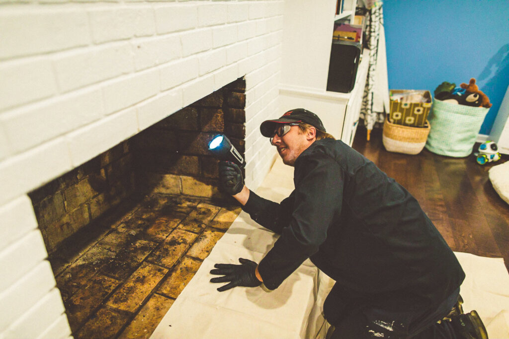 A chimney sweep from Soot Busters inspecting a fireplace with a flashlight in a home in Birmingham, AL.