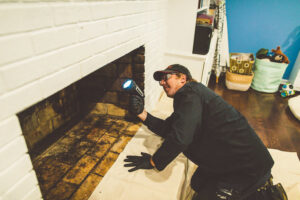 A chimney sweep from Soot Busters inspecting a fireplace with a flashlight in a home in Birmingham, AL.