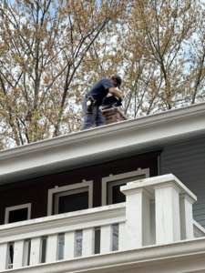 A chimney sweep working on a chimney on a roof for Chimney Cricket Cleaning Service in Marshfield, MO