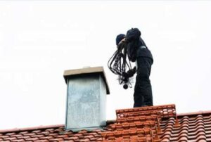 A chimney sweep technician from 832 Home Service on a roof, cleaning the chimney flue in Houston, TX.