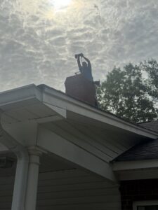A Soot Masters Chimney Service LLC professional performing a chimney sweep from the rooftop in Jackson, MS.