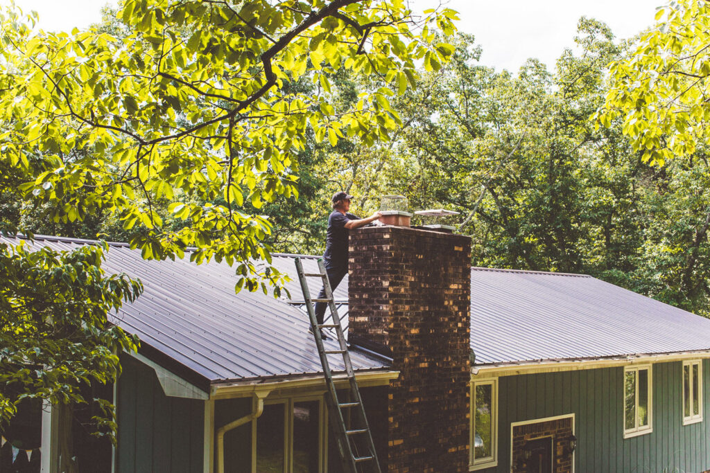 A chimney sweep from Soot Busters on a ladder on a roof, performing work on a brick chimney in Birmingham, AL.